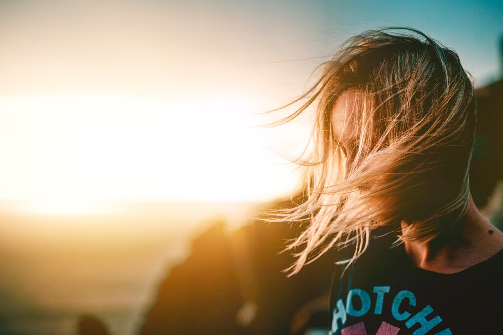 chica rubia mirando al suelo y en una puesta de sol